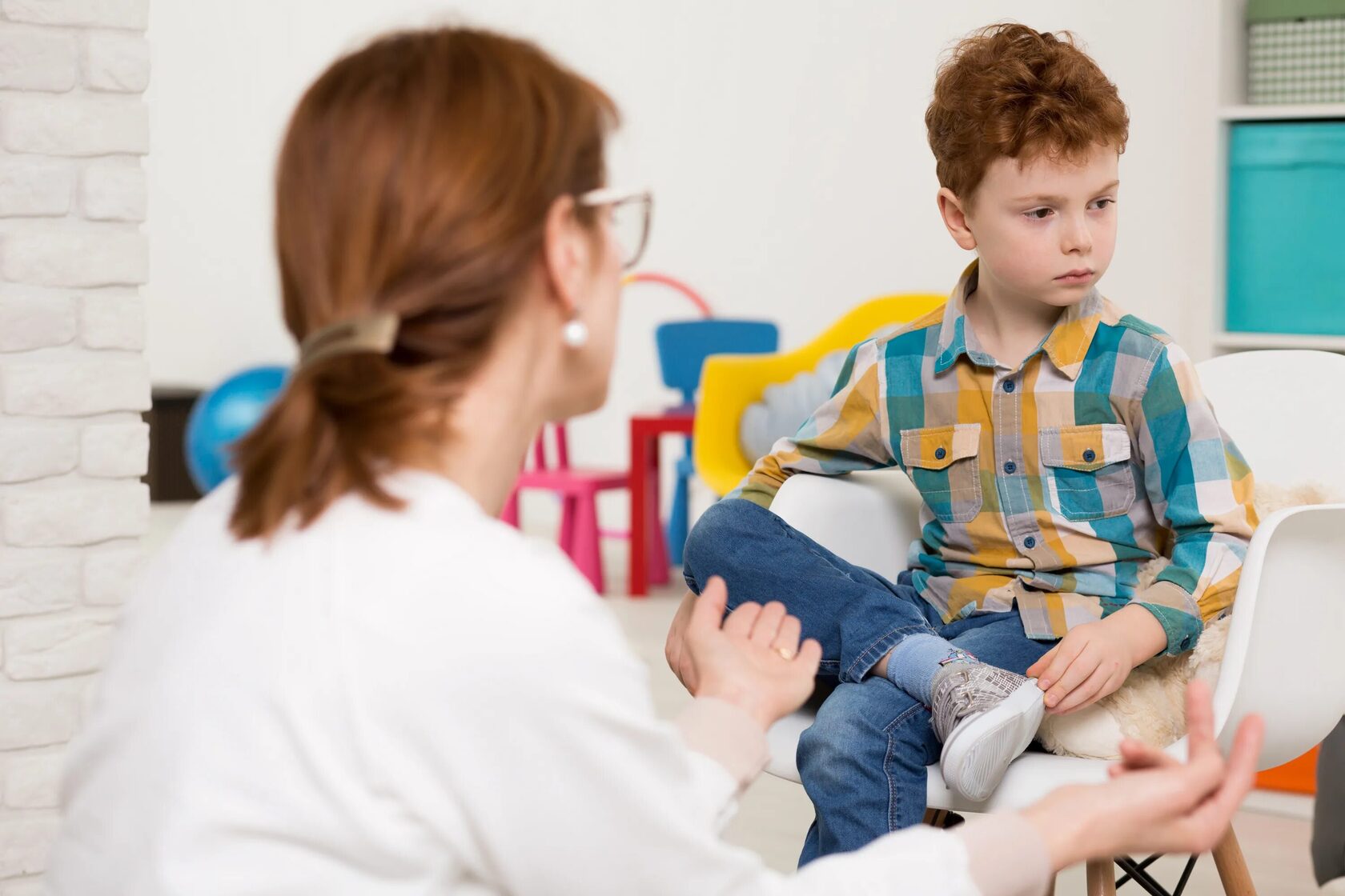 Young boy looking away while a therapist speaks to him during a therapy session.